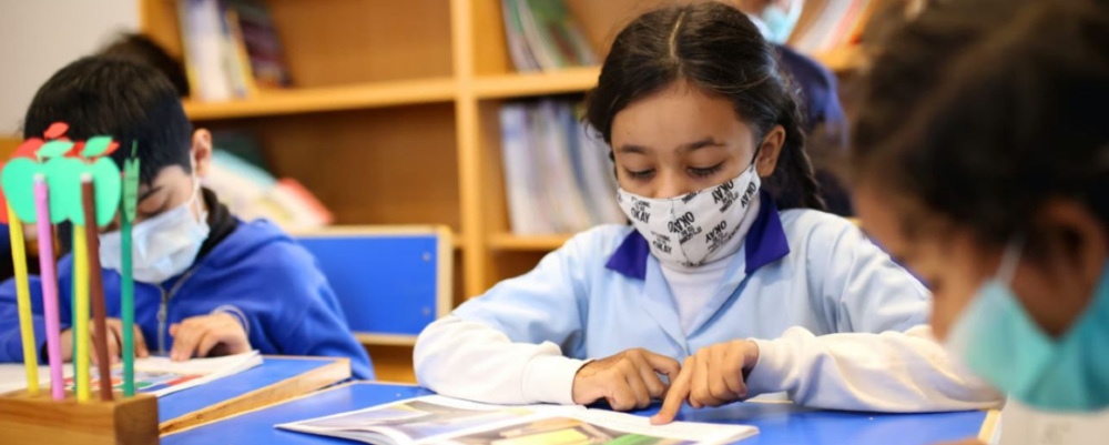 three kids in medical masks working at an elementary school table