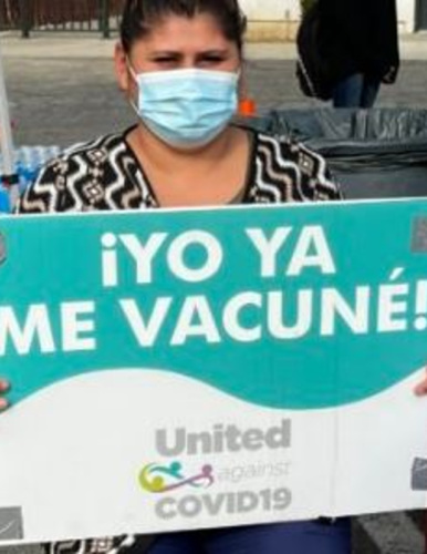 a UAC volunteer at a vaccine clinic holding a sign in Spanish reading "Yo Ya Me Vacune"