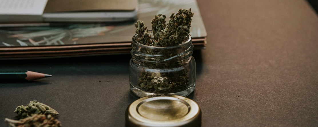 cannabis in a jar on a table with a notepad
