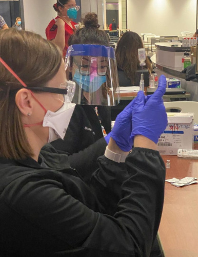 Two women health workers in medical masks and shields preparing vaccinations