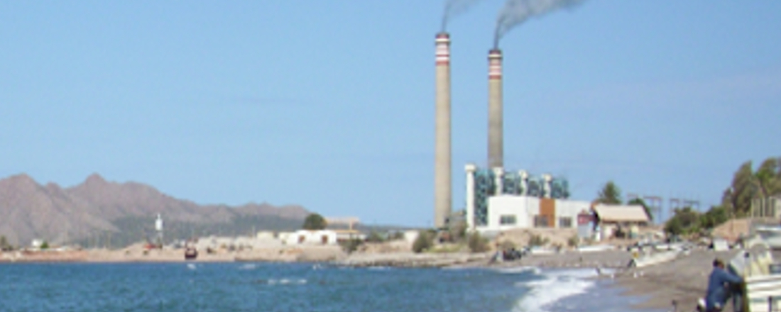 Two tall, polluting factory pipes on an ocean shoreline