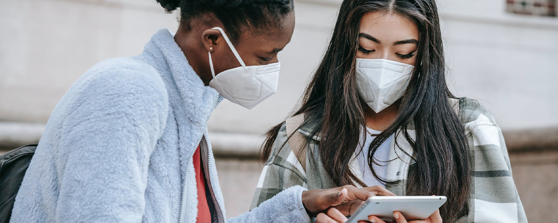 two teens wearing masks staring at tablet