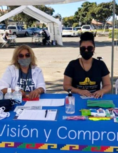 Two women in medical masks tabling at an outdoor vaccine event