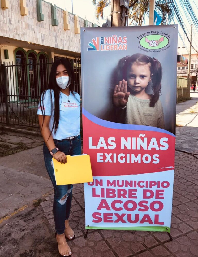 A Rise Up Girl Leader with a large poster calling for an end to sexual harassment and violence