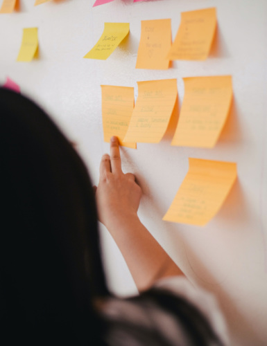 A woman pointing to post-it notes on a whiteboard