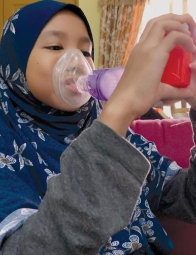 Asian girl using inhaler with spacer