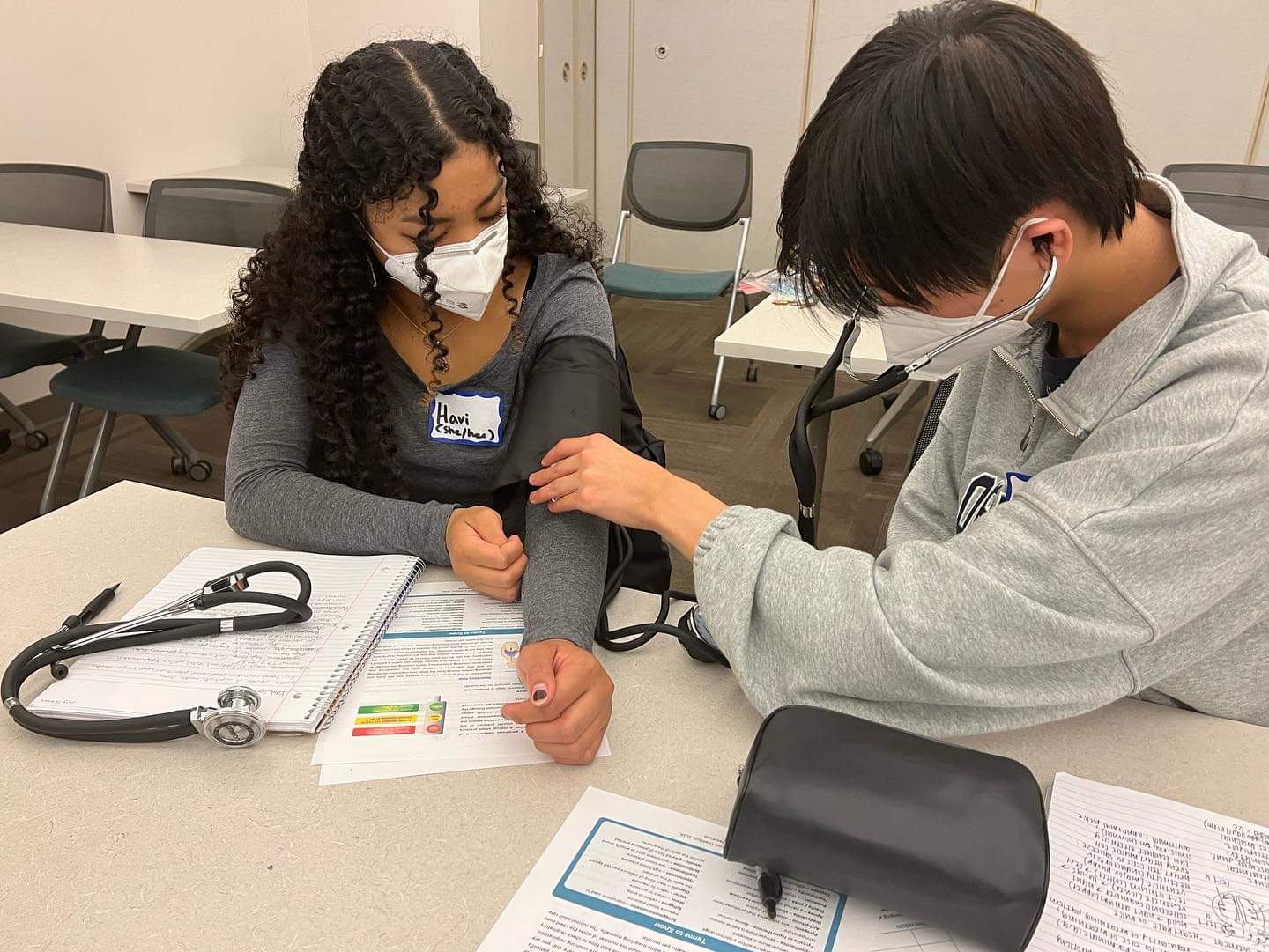 Two FACES students learning how to check blood pressures using blood pressure cuffs and stethoscopes