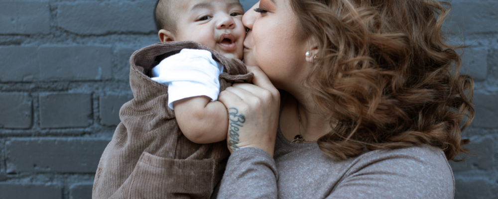 Latinx mother holding baby boy and kissing him on the cheek