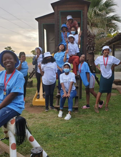 A group of girl leaders in South Africa sitting outside on a play structure and smiling