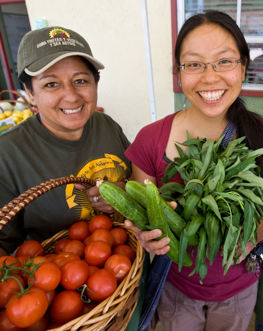 Two women holding vegetables at an outdoor farmer's market