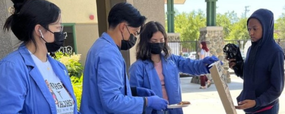 high school students in medical jackets at outdoor covid prevention table