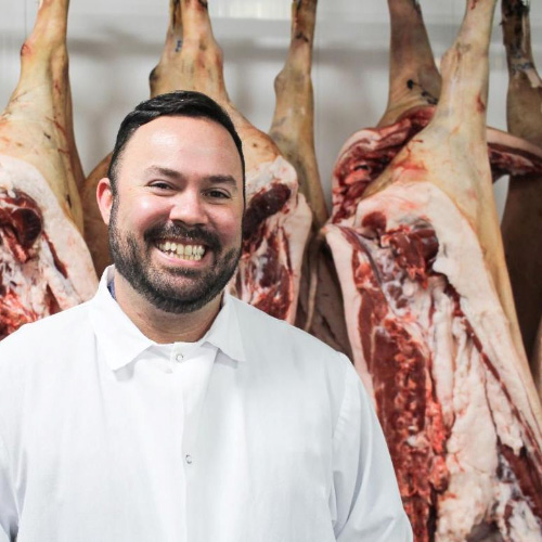 person smiling in front of meat