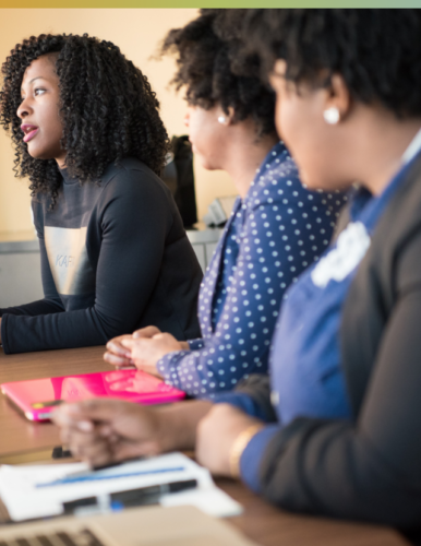 Three African American women sitting next to each other in a meeting and talking