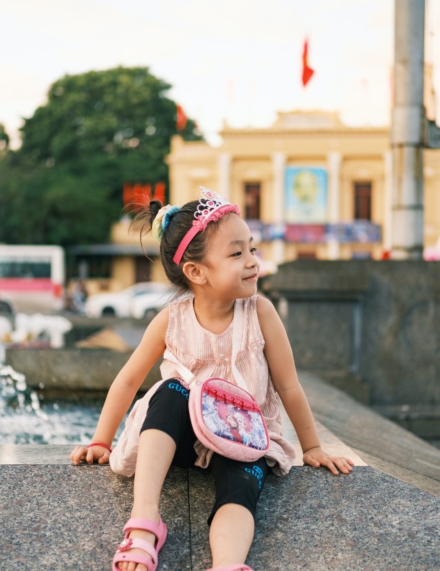 little girl smiling, sitting near fountain