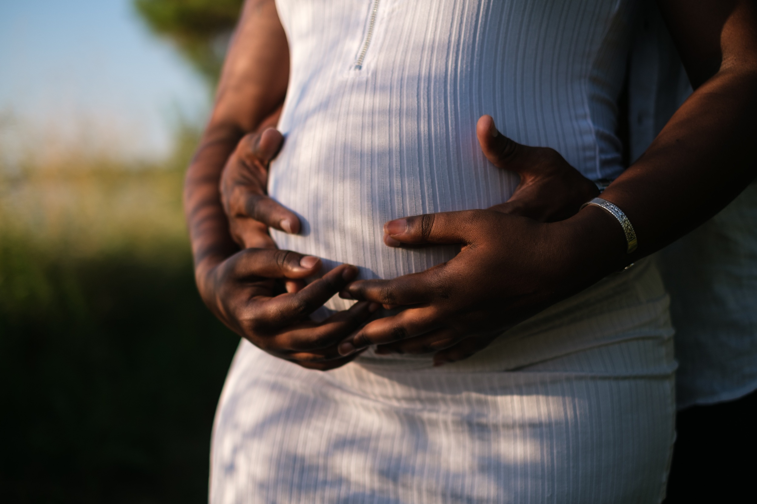 Pregnant African American woman holding her stomach with African American partner standing behind her holding her stomach