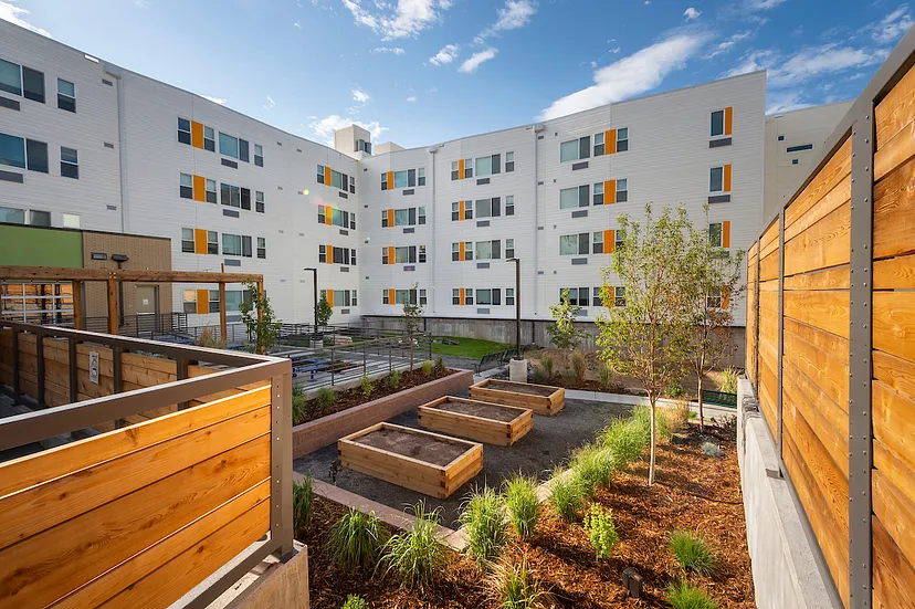 A row of planter boxes and a high fence outline a space outside a large multi-unit housing complex.