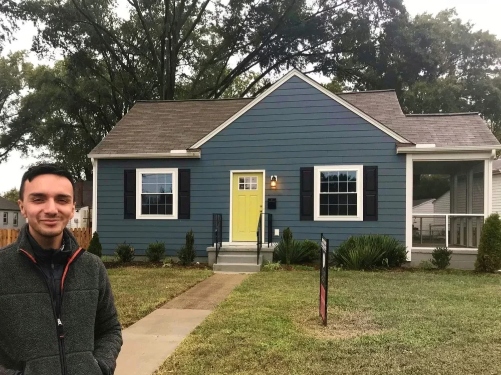 A man stands at the end of a walkway in front of a single family home.