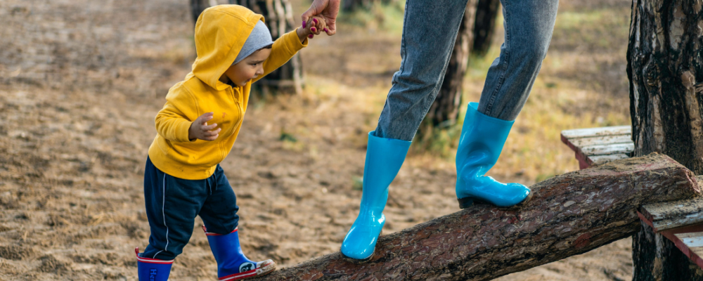 mother holding sons hand while climbing on a log at the park