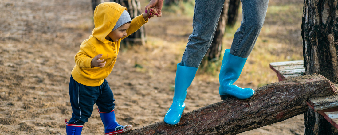 mother holding sons hand while climbing on a log at the park