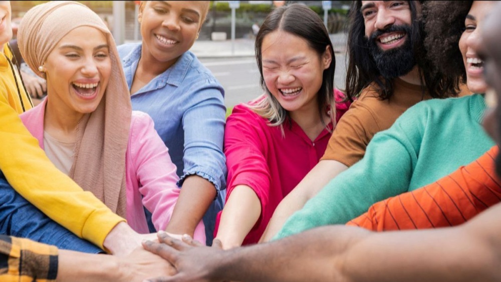 a group of people in brightly colored shirts put their hands into the center of the group.