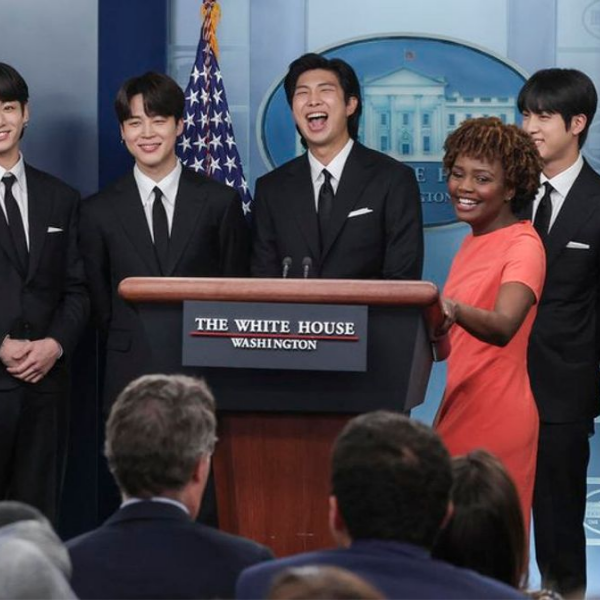 KPop musicians stand next to U.S. Press Secretary Karine Jean-Pierre behind a podium in the White House press room.