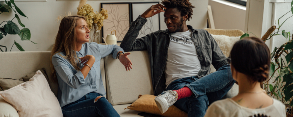 two women and a man sitting on a couch talking to each other