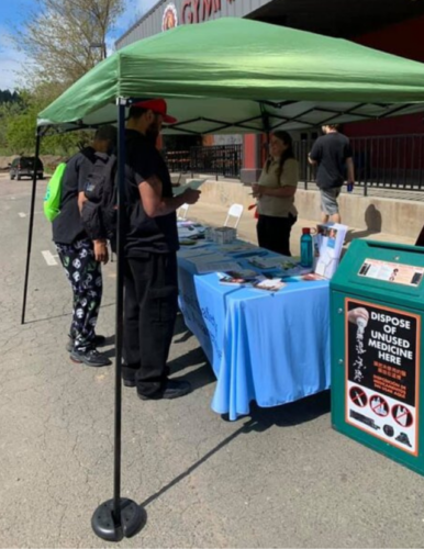 community members at a booth with drop off box offering disposal of unused medicine