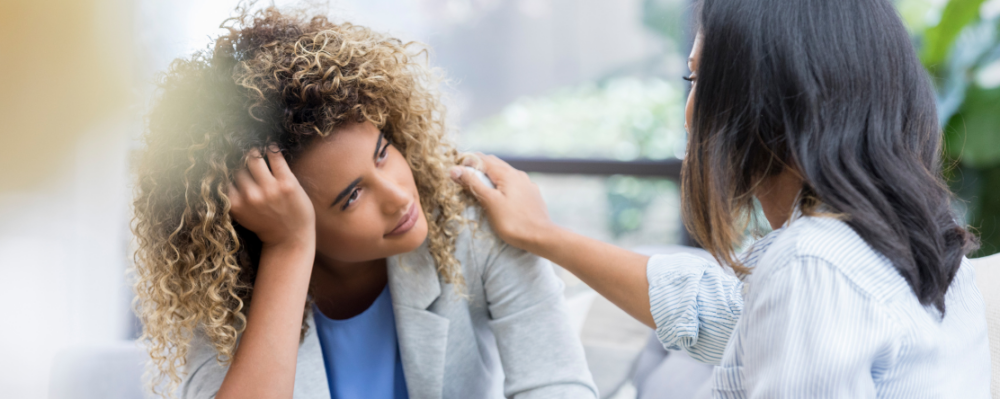 Two women in conversation, one with her arm reaching across to touch the other's shouler