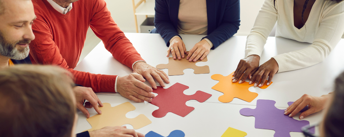 Group of people holding large puzzle pieces on a table