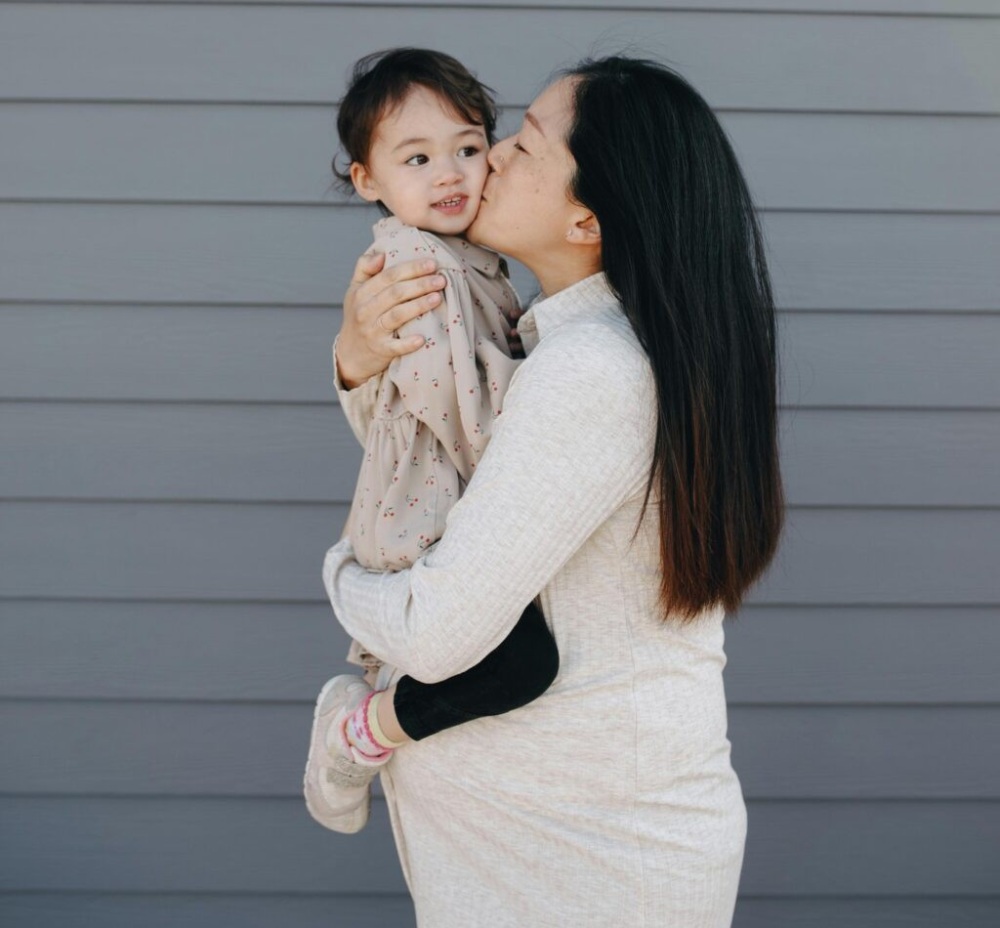 pregnant woman holds and kisses young child on the cheek