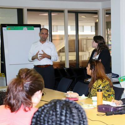 man standing in front of whiteboard lecturing to people sitting in tables