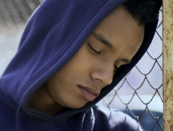 person in a hoodie leaning their head against a chain link fence