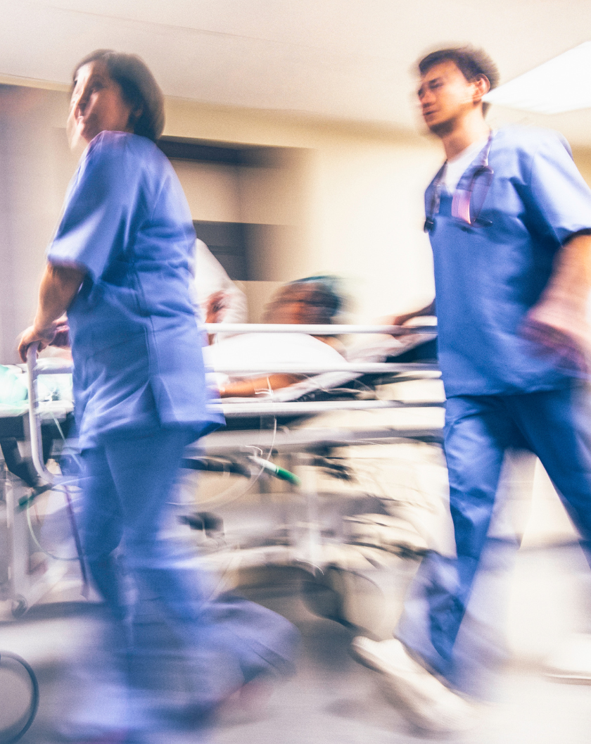 healthcare workers rushing a patient on a gurney in the emergency room