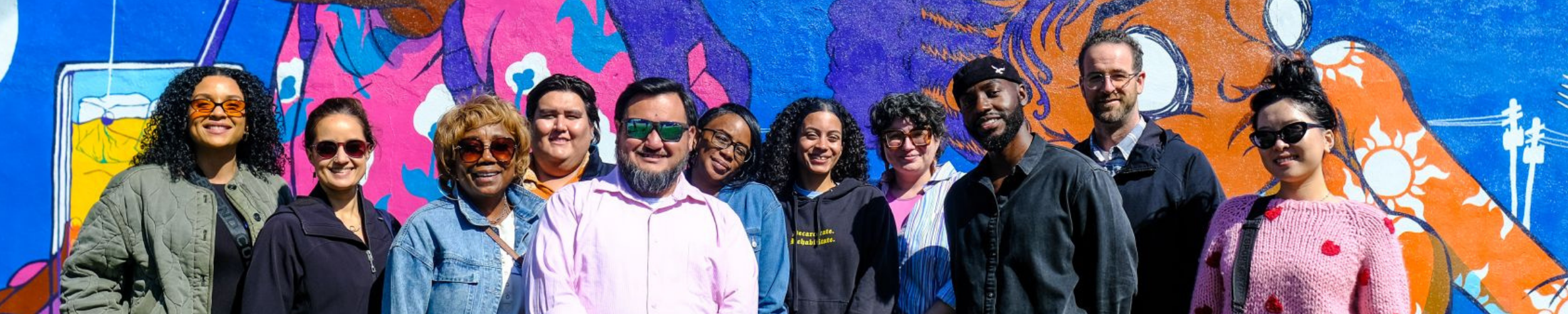 a group of people standing in front of an outdoor mural