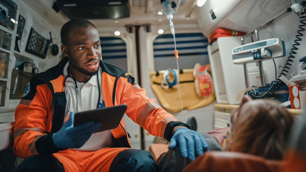 an EMT holds tablet and treats patient in an ambulence